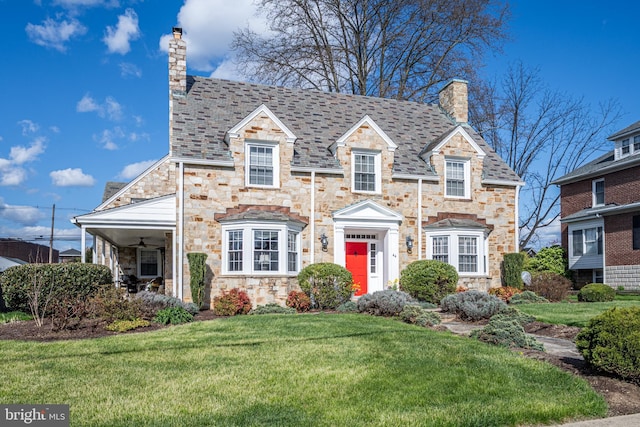 view of front of home featuring ceiling fan, a high end roof, a chimney, a front yard, and stone siding