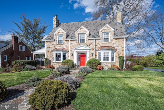 cape cod home with a high end roof, a chimney, a front lawn, and stone siding