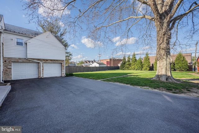 view of yard with an attached garage, fence, and aphalt driveway