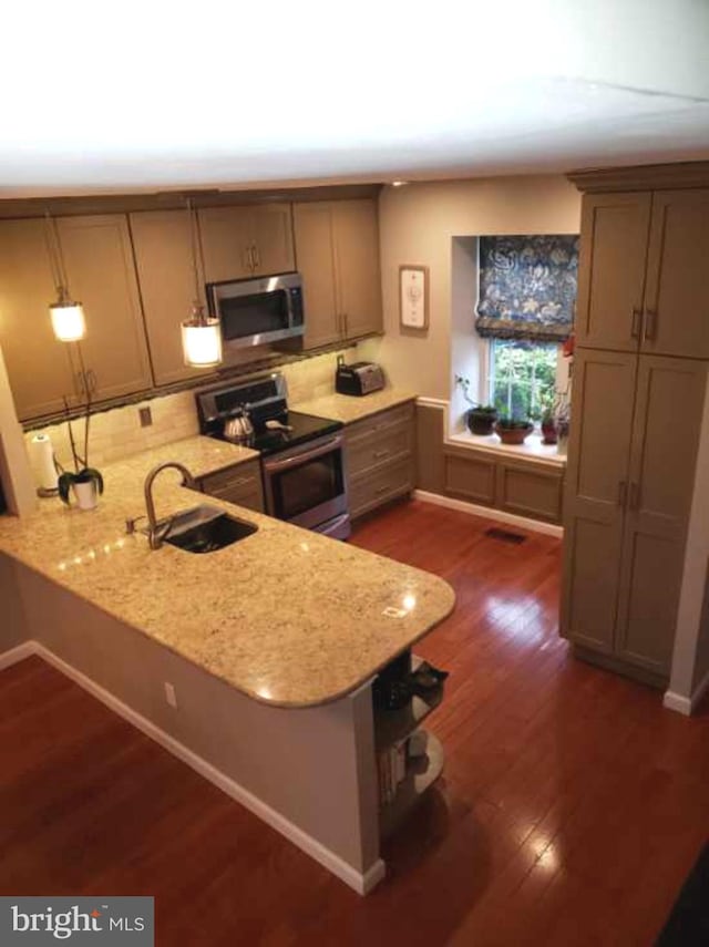 kitchen featuring light stone counters, stainless steel appliances, a sink, a peninsula, and dark wood-type flooring