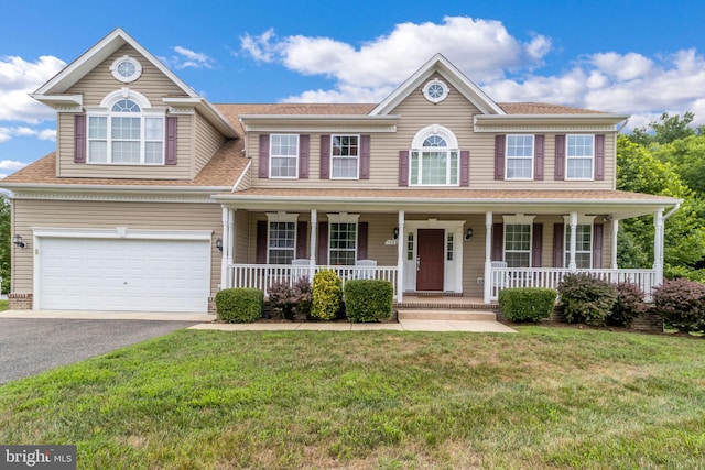 colonial home featuring a porch, a front lawn, an attached garage, and driveway