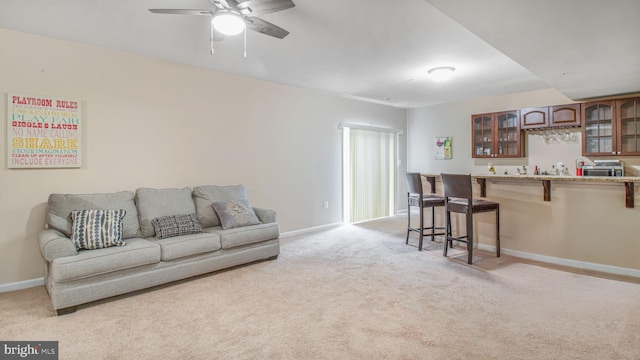 living room with baseboards, wet bar, ceiling fan, and light carpet