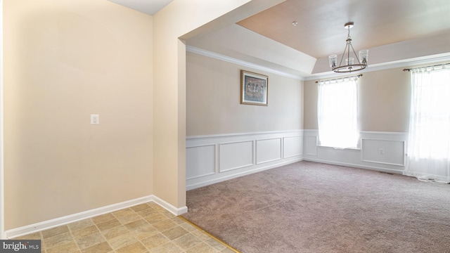 empty room featuring a raised ceiling, wainscoting, a chandelier, and a wealth of natural light