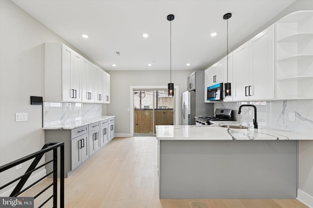 kitchen with a peninsula, open shelves, light stone counters, a sink, and stainless steel appliances