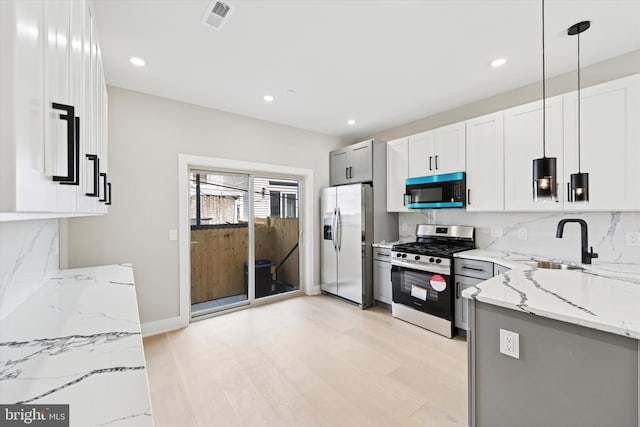 kitchen with light wood-type flooring, light stone counters, visible vents, stainless steel appliances, and a sink