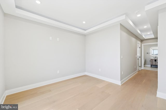 unfurnished room with a raised ceiling, light wood finished floors, and baseboards
