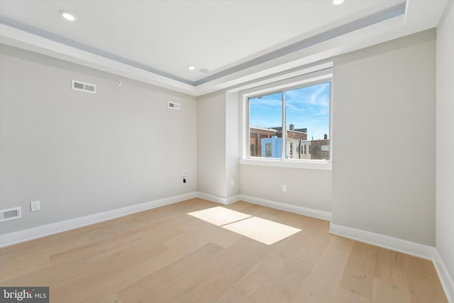 empty room with visible vents, baseboards, a tray ceiling, light wood finished floors, and recessed lighting