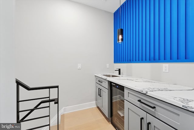 kitchen with baseboards, a sink, wine cooler, light wood finished floors, and light stone counters
