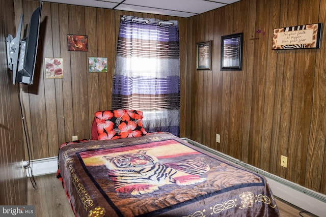 bedroom featuring wood walls, wood finished floors, and baseboard heating