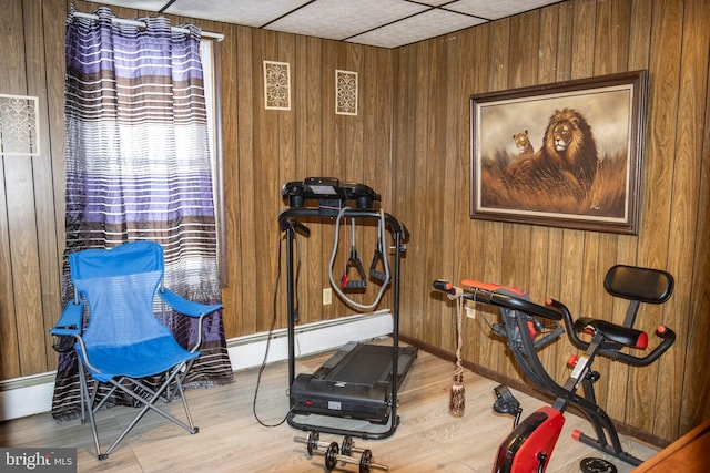 exercise room with wooden walls, a baseboard radiator, and wood finished floors