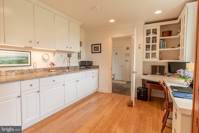 kitchen with light wood-type flooring, ornamental molding, a sink, and white cabinetry