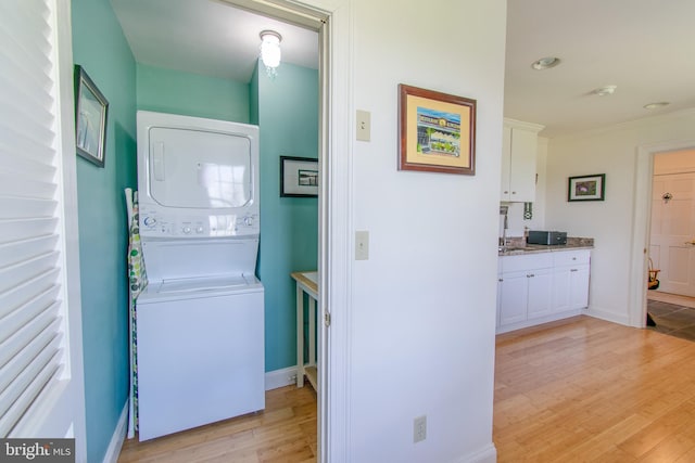 clothes washing area featuring baseboards, recessed lighting, light wood-style floors, stacked washer / dryer, and laundry area