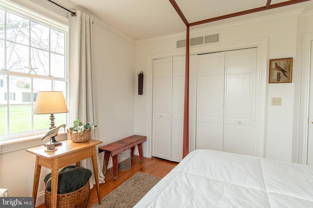 bedroom with visible vents, a closet, crown molding, and wood finished floors