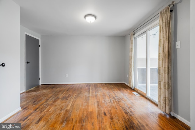 empty room featuring visible vents, baseboards, wood finished floors, and a healthy amount of sunlight