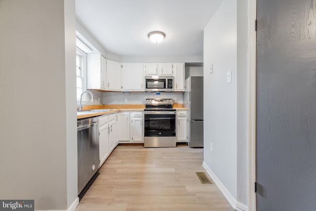 kitchen featuring light wood-style flooring, light countertops, white cabinetry, appliances with stainless steel finishes, and a sink