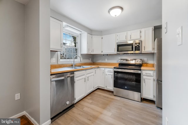 kitchen featuring baseboards, a sink, white cabinetry, stainless steel appliances, and light wood-style flooring