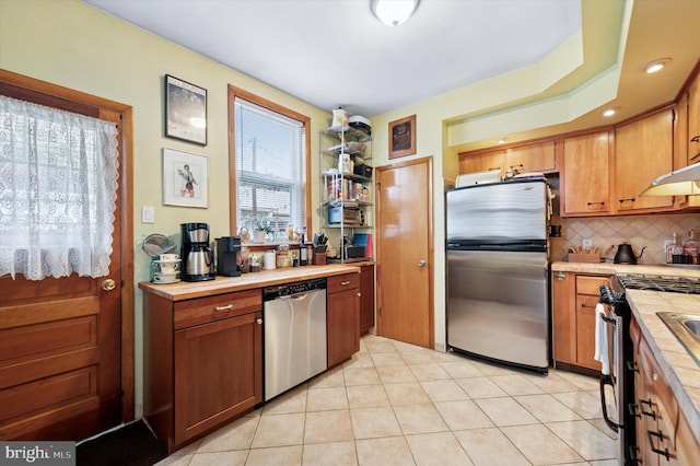 3257 Almond St, Philadelphia, PA 19134 - kitchen with stainless steel appliances, tasteful backsplash, brown cabinets, under cabinet range hood, and light tile patterned floors