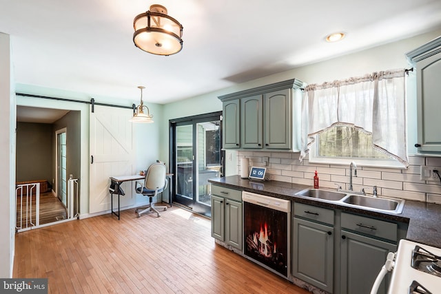 kitchen with white gas range oven, dark countertops, dishwashing machine, a sink, and gray cabinetry