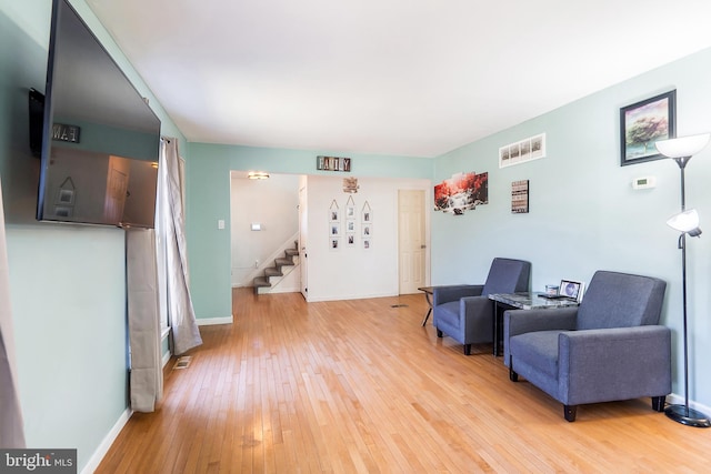 living area featuring baseboards, visible vents, light wood-style flooring, and stairway