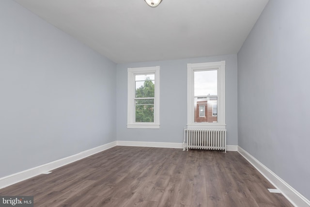 spare room with baseboards, dark wood-style floors, and radiator