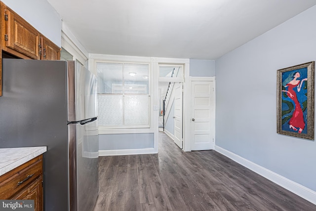 kitchen with brown cabinetry, light countertops, baseboards, freestanding refrigerator, and dark wood-type flooring