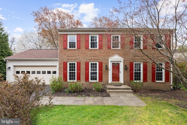 colonial inspired home with an attached garage, roof with shingles, aphalt driveway, and brick siding