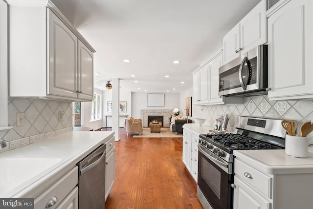 kitchen with white cabinets, stainless steel appliances, a ceiling fan, and a fireplace