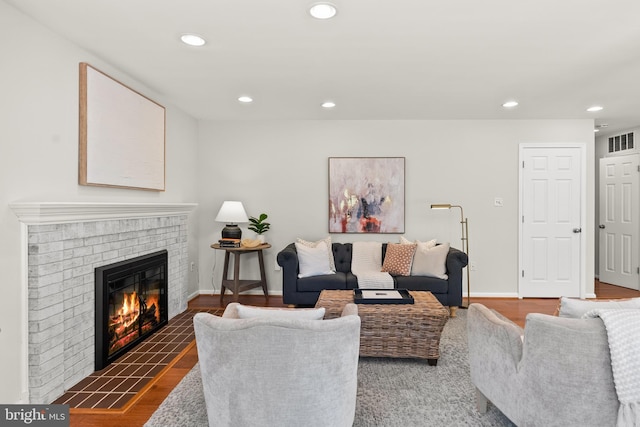 living area featuring wood finished floors, baseboards, a brick fireplace, visible vents, and recessed lighting
