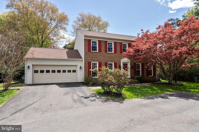 colonial home featuring driveway, brick siding, a front yard, and a garage