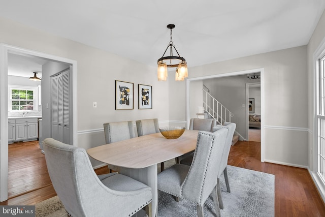 dining space with baseboards, wood finished floors, stairs, and a notable chandelier