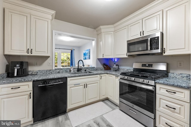 kitchen with stainless steel appliances, light wood-style flooring, a sink, and light stone counters