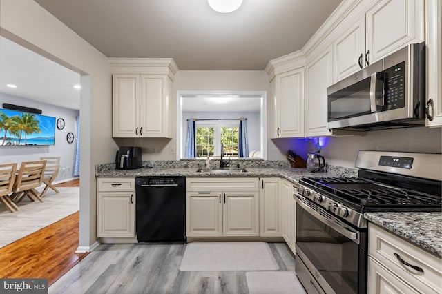kitchen with white cabinets, light stone counters, stainless steel appliances, a sink, and light wood-style floors