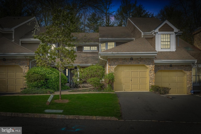 townhome / multi-family property with aphalt driveway, stone siding, roof with shingles, a front yard, and a garage
