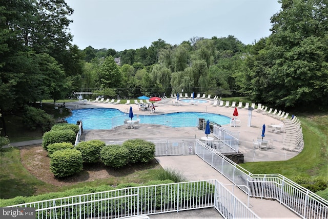 community pool featuring fence, a patio area, and a forest view