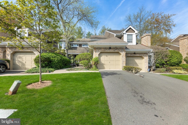 townhome / multi-family property with aphalt driveway, a shingled roof, a front lawn, stone siding, and a garage