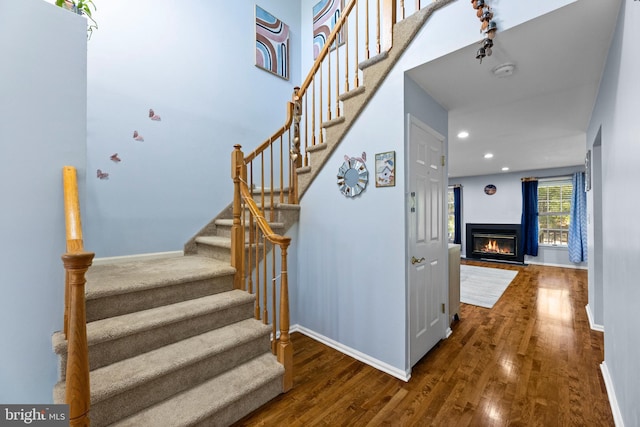 stairway featuring a glass covered fireplace, wood finished floors, baseboards, and recessed lighting