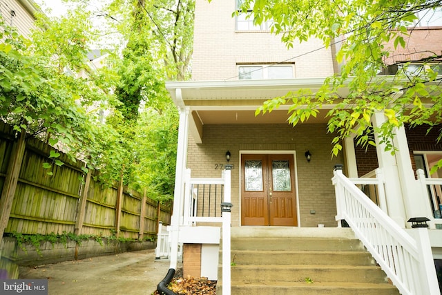 entrance to property with brick siding, fence, and covered porch