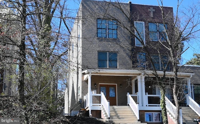 view of front of home featuring brick siding, covered porch, and stairway