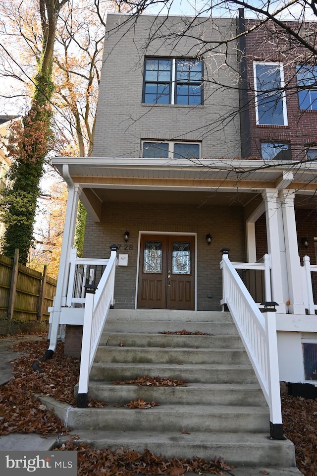 view of exterior entry with a porch, fence, and brick siding