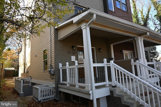 view of side of property featuring covered porch and brick siding