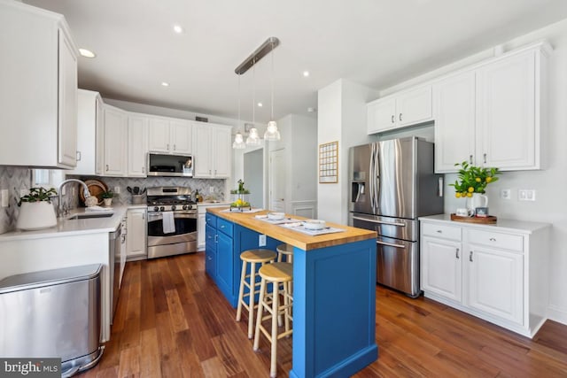 kitchen featuring stainless steel appliances, a kitchen island, wooden counters, white cabinets, and a sink