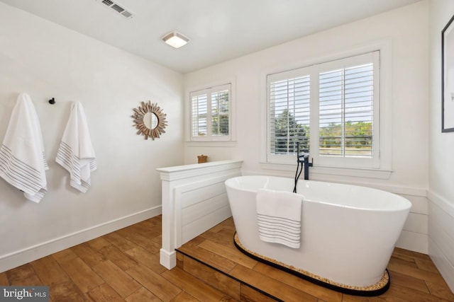 bathroom featuring visible vents, a freestanding tub, and wood finished floors