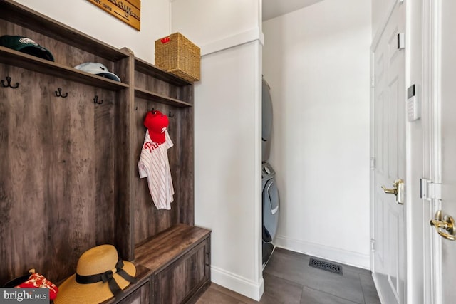 mudroom featuring stacked washer and dryer, baseboards, dark tile patterned flooring, and visible vents
