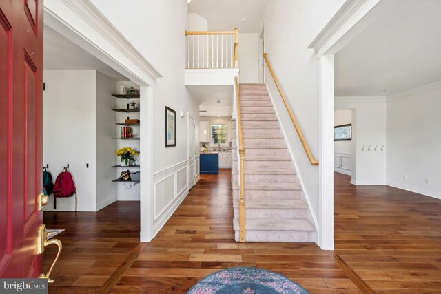 foyer entrance featuring wood finished floors, crown molding, and stairs