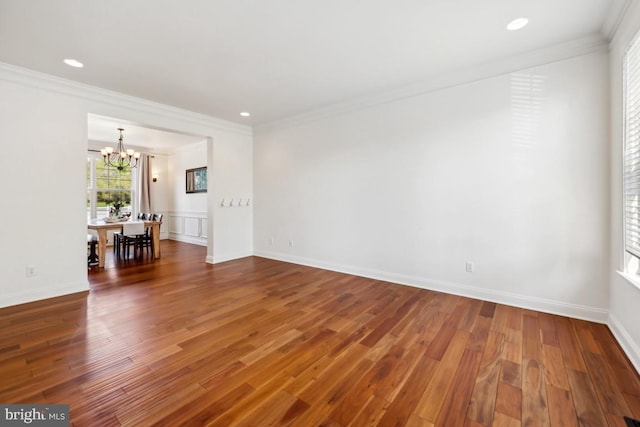 spare room with baseboards, wood finished floors, a chandelier, and ornamental molding