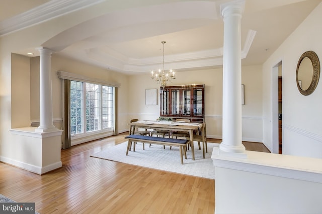 dining space featuring light wood finished floors, a raised ceiling, baseboards, decorative columns, and a chandelier