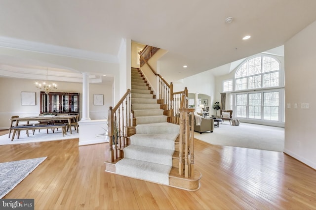 stairs featuring hardwood / wood-style floors, ornate columns, arched walkways, an inviting chandelier, and recessed lighting