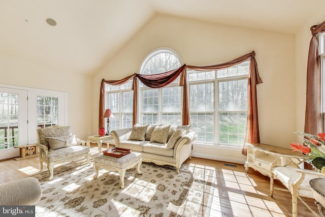 living room with high vaulted ceiling, a wealth of natural light, visible vents, and light wood-type flooring