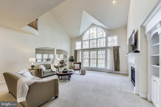carpeted living area featuring high vaulted ceiling, a fireplace with flush hearth, a healthy amount of sunlight, and decorative columns