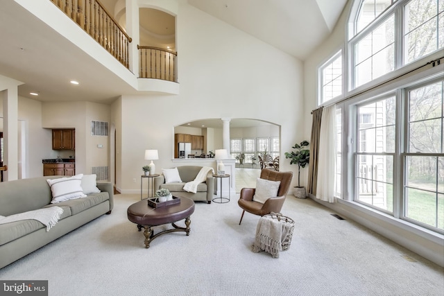carpeted living room featuring a high ceiling, arched walkways, baseboards, visible vents, and ornate columns